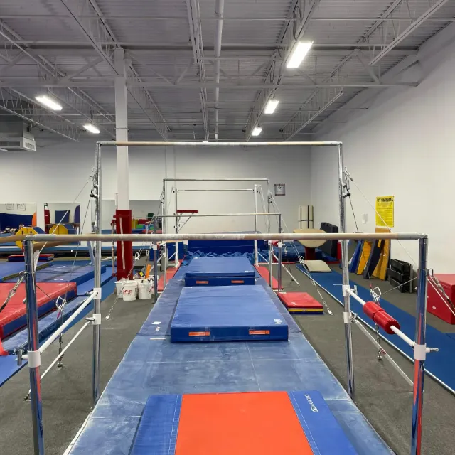 An indoor gymnastics training center with parallel bars, mats, and other gymnastic equipment in an organized and professional setup.