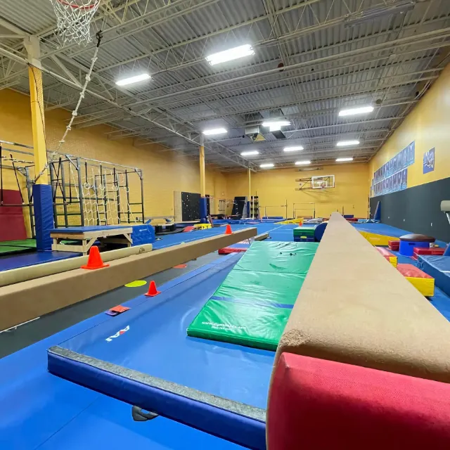 A spacious indoor gymnastics training area with various equipment including balance beams, mats, and bars.