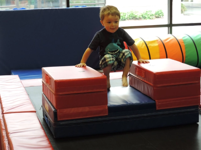 A little boy with a joyful expression jumping between foam blocks in a gymnastics center.