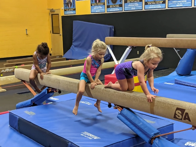 Three young girls practicing on balance beams in a gymnastics gym, focusing intently on their form.