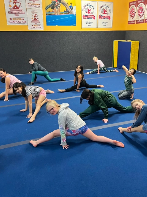 A diverse group of children smiling and stretching on a blue gym floor during a gymnastics class.